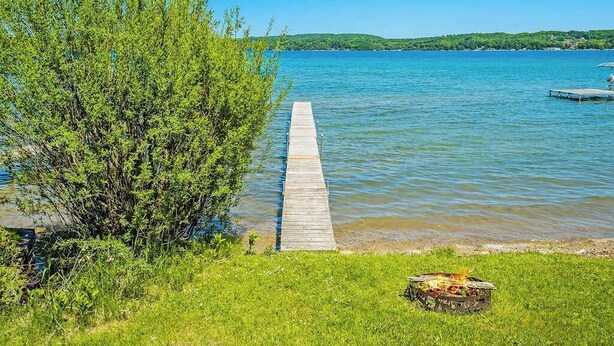 Eine Holzsteg, der sich in ruhiges Wasser erstreckt, umgeben von Grünpflanzen und einem klaren Himmel.