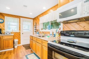 A kitchen with wooden cabinets, a stove, a microwave, and a window with curtains. - Pleasant lake house w/ free cable, guest kayak, set on trail - dogs allowed (Beulah)