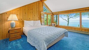 Una camera da letto con un letto grande, un comodino, una lampada e vista mare attraverso ampie finestre.