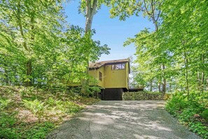 A house surrounded by dense green foliage, with a gravel path leading to the entrance.