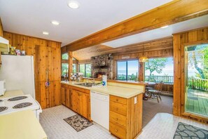 A kitchen with wooden cabinets, a stone fireplace, a large island, and a view of the outdoors.