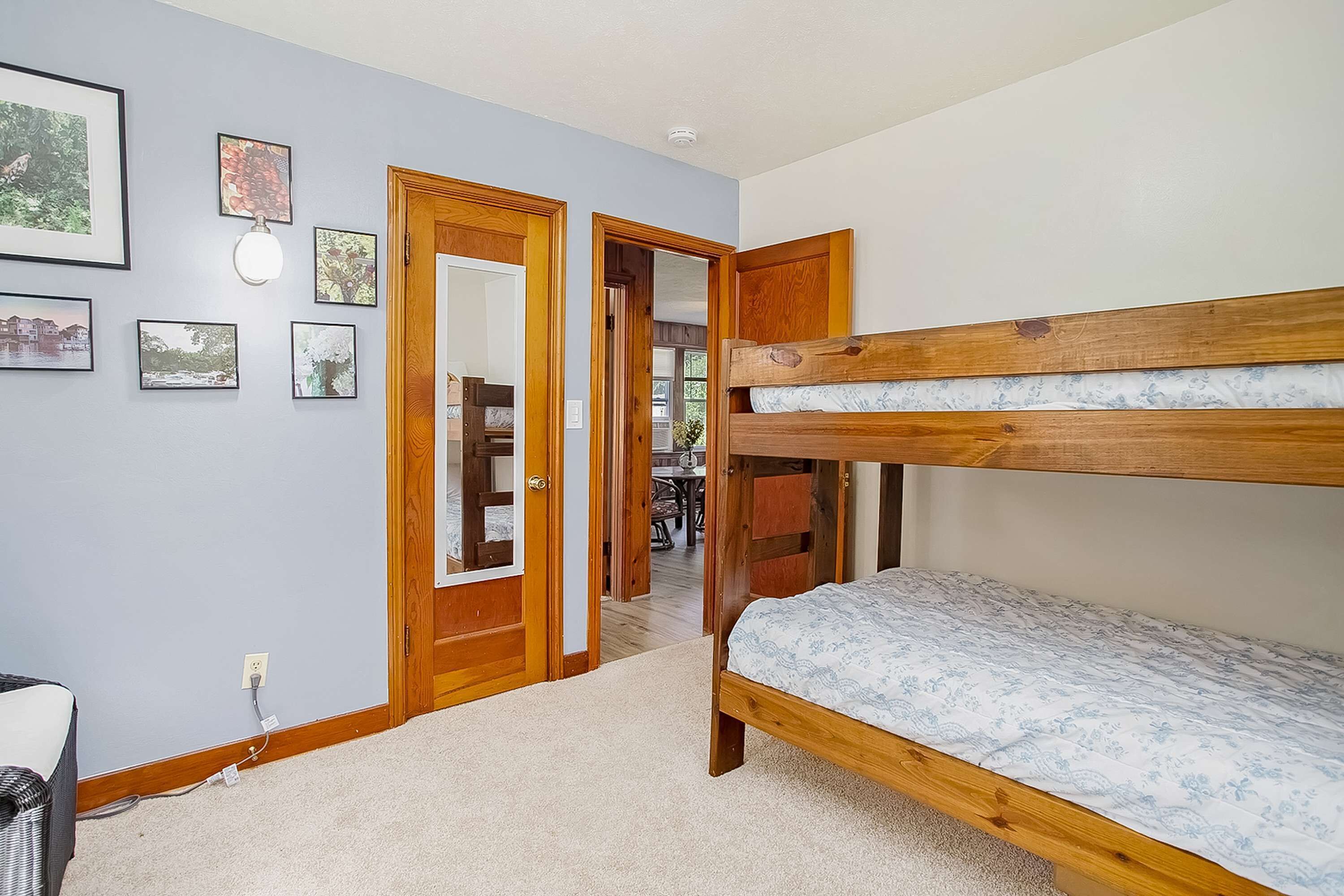 A room with a bunk bed, a door leading to another room, and framed pictures on the wall.