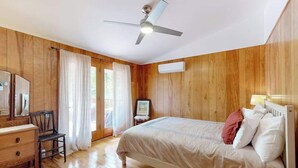 A bedroom with wooden walls, a bed, a desk, a chair, a ceiling fan, and a window with curtains. - Dog-friendly home in the perfect location with enclosed yard, streaming, & W/D (Union Pier)