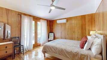 A bedroom with wooden walls, a bed, a desk, a chair, a ceiling fan, and a window with curtains.