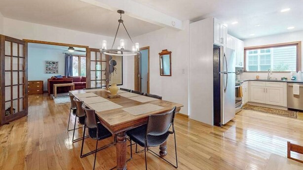 A spacious dining area with a wooden table and chairs, a chandelier, and a kitchen with white cabinets and a refrigerator. - Dog-friendly home in the perfect location with enclosed yard, streaming, & W/D (Union Pier)