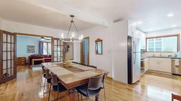 A spacious dining area with a wooden table and chairs, a chandelier, and a kitchen with white cabinets and a refrigerator.