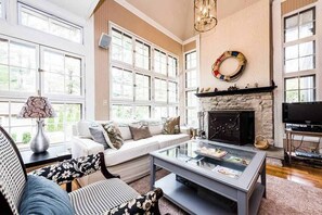 A living room with a fireplace, large windows, a sofa, and a coffee table. - Secluded, charming home with in-ground pool, hot tub, firepit & high-speed WiFi (Union Pier)