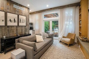 A living room with a sofa, armchair, and a coffee table. There is a fireplace, a window with curtains, and a bookshelf. - Custom-design luxury home with lovely patio, firepit - walk to beaches (Union Pier)