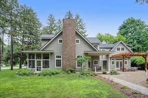 A two-story house with a brick chimney, large windows, and a covered porch. - Custom-design luxury home with lovely patio, firepit - walk to beaches (Union Pier)