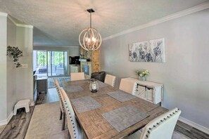 A dining area with a wooden table, chairs, a chandelier, and a painting on the wall. - Serene Home with Fire pit, Gas Grill, WIFI & Close to Beach (Three Oaks)