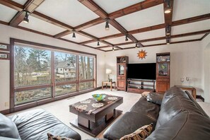A living room with a large window, a fireplace, a television, and a leather couch. - Dog-friendly home near Lake Michigan with patio & firepit (South Haven)