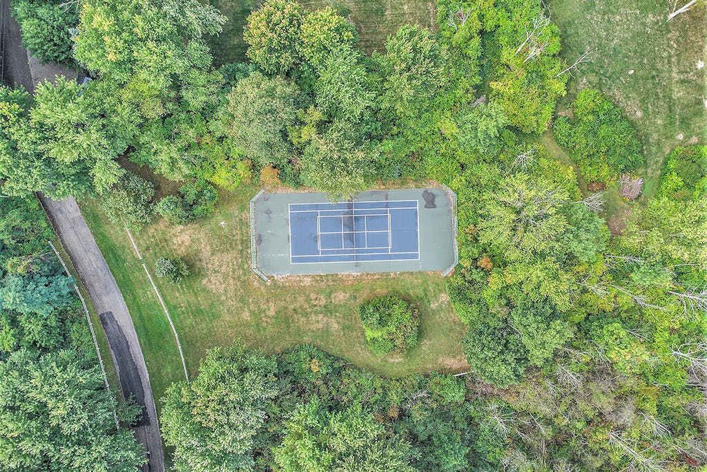 Ovenudblik over en tennisbane omgivet af frodig vegetation.