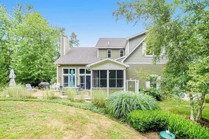 Ein zweistöckiges Haus mit überdachter Terrasse, umgeben von einem gepflegten Garten und Bäumen.