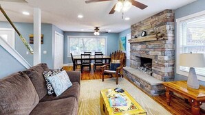 Una sala de estar con chimenea de piedra, ventilador de techo, mesa de comedor y sofá.