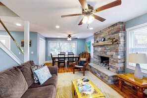 Una sala de estar con chimenea de piedra, ventilador de techo, mesa de comedor y sofá.