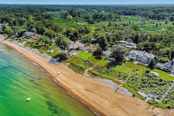 An aerial view of a coastal residential area with houses, a beach, and clear green water.