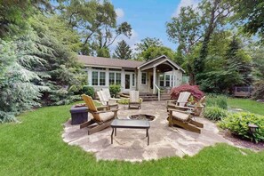 Ein Haus mit einer Terrassenanlage, die Gartenmöbel und eine Feuerstelle bietet.