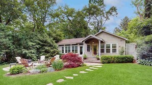 Ein Haus mit Veranda, Rasen und Garten mit verschiedenen Pflanzen und einem roten Busch.
