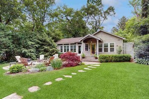 Ein Haus mit Veranda, Rasen und Garten mit verschiedenen Pflanzen und einem roten Busch.