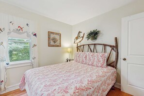 A bedroom with a bed, a window with curtains, a wall-mounted lamp, and a door. - Adorable Downtown Cottage with Firepit, Fireplace, & Yard - Walk Everywhere (New Buffalo)