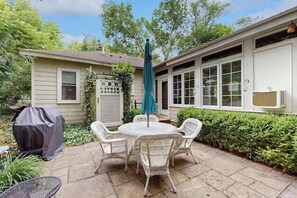 A patio with a round table and chairs, an umbrella, and a grill. - Adorable Downtown Cottage with Firepit, Fireplace, & Yard - Walk Everywhere (New Buffalo)