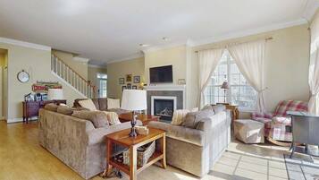 A spacious living room with a fireplace, a staircase, and a large window with curtains.