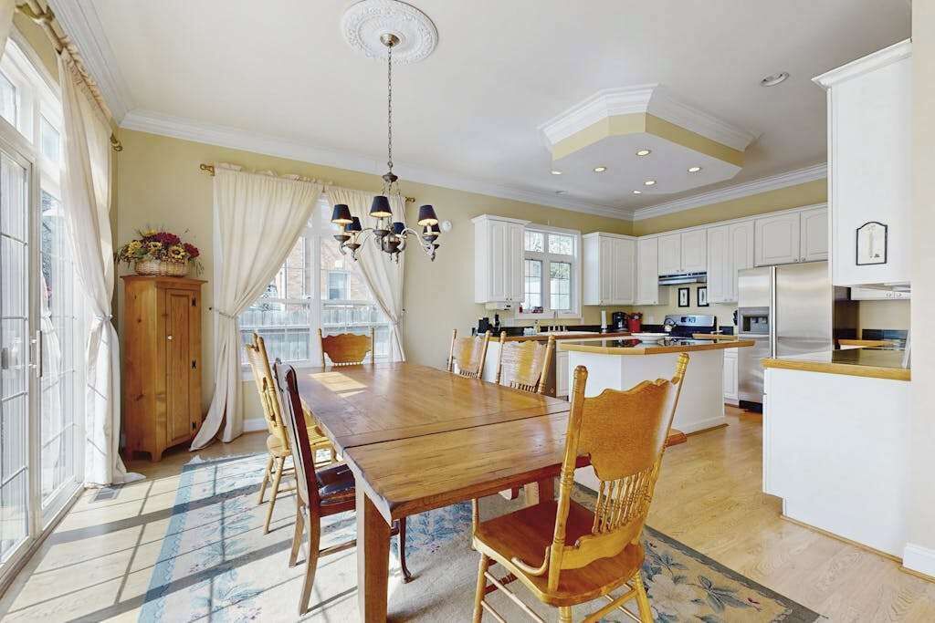 A spacious kitchen with white cabinets, a wooden dining table, and a chandelier.