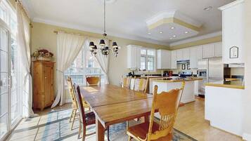 A spacious kitchen with white cabinets, a wooden dining table, and a chandelier.