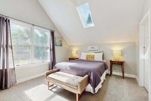 Un dormitorio con cama, banca, ventana y tragaluz.