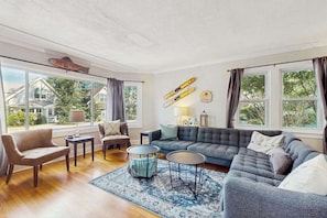 A living room with a sofa, chairs, a coffee table, and a rug. There are windows with curtains, a bicycle, and a fish decoration on the wall. - Enjoy a scenic getaway, a relaxing hot tub, and seasonal comfort. (New Buffalo)