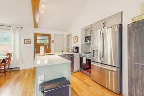 A modern kitchen with stainless steel appliances, a wooden dining table, and a large window.