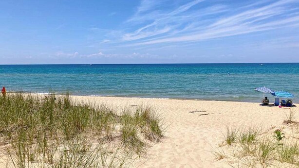 En strand med klare himmel, sandet bredde og nogle få strandparasoller.