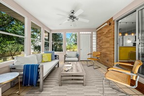 A sunroom with a sofa, coffee table, and chairs, large windows, and a ceiling fan. - Steps to Ridge Road Beach Renovated Home w/ Private Hot Tub, Firepit & Porch (Grand Beach)