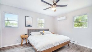 Ein Schlafzimmer mit einem Bett, einem Nachttisch, einem Deckenventilator und zwei Fenstern.