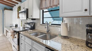 A kitchen with white cabinets, a stainless steel sink, granite countertops, and a window with blue shutters.