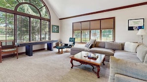 A spacious living room with large windows, a sofa, a coffee table, and a bench. - Golf Front Home with Course View, WiFi, Patio & Grill (Benton Harbor)
