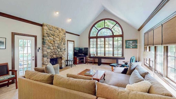 A spacious living room with a stone fireplace, large windows, and a high ceiling. - Golf Front Home with Course View, WiFi, Patio & Grill (Benton Harbor)