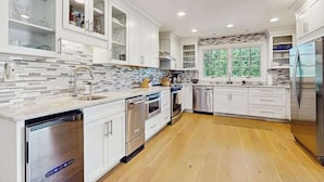 A modern kitchen with white cabinetry, a tiled backsplash, stainless steel appliances, and a window with a view of greenery. - Golf Front Home with Course View, WiFi, Patio & Grill (Benton Harbor)