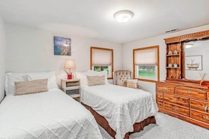 A bedroom with two beds, a dresser, a chair, and a window with blinds.
