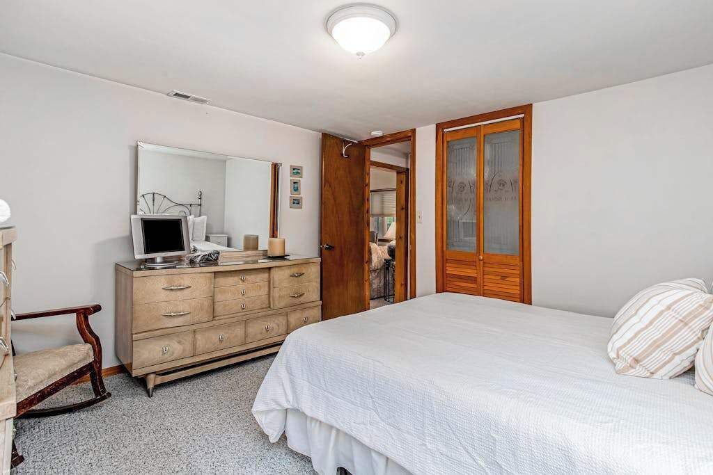 Ein Schlafzimmer mit Bett, Schminktisch, Spiegel und einer Tür zu einem weiteren Raum.