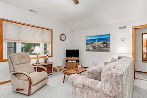 A living room with a sofa, armchair, TV, and a painting on the wall.
