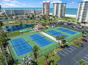 Ett hotell med flera våningar, en tennisbana, en swimmingpool och utsikt över havet.