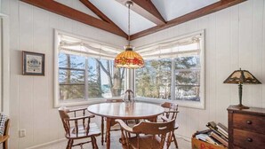 Un comedor con una mesa redonda, sillas de madera, una lámpara colgante de vitral y vistas amplias a través de grandes ventanales.