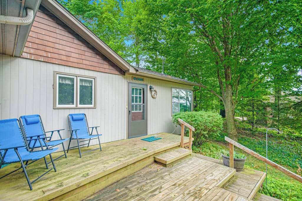 Une terrasse en bois avec des chaises bleues, un petit porche et une porte avec une boîte aux lettres.