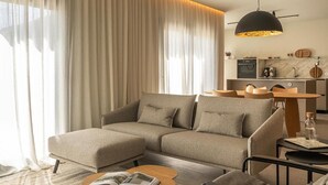 A modern living room with a sectional sofa, a small round coffee table, and a dining area with a table and chairs. - Designer House Laloma (Málaga)