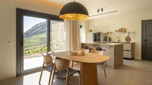 A modern kitchen with a dining area, large windows, and a view of a mountainous landscape. - Designer House Laloma (Málaga)