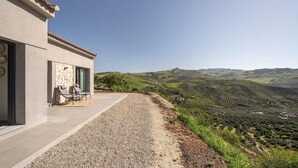 A modern building with a patio, outdoor seating, and a view of rolling hills. - Designer House Laloma (Málaga)