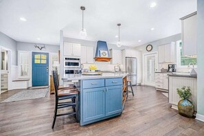 A modern kitchen with white cabinets, a blue island, and pendant lighting. - Lakeview home with beach access, private pickleball court, firepits & fireplace (South Haven)