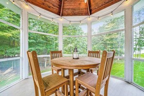 A round wooden table with chairs, a lantern, and large windows with a view of greenery. - Lakeview home with beach access, private pickleball court, firepits & fireplace (South Haven)