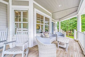 A covered porch with white wicker furniture and a wooden table. - Lakeview home with beach access, private pickleball court, firepits & fireplace (South Haven)